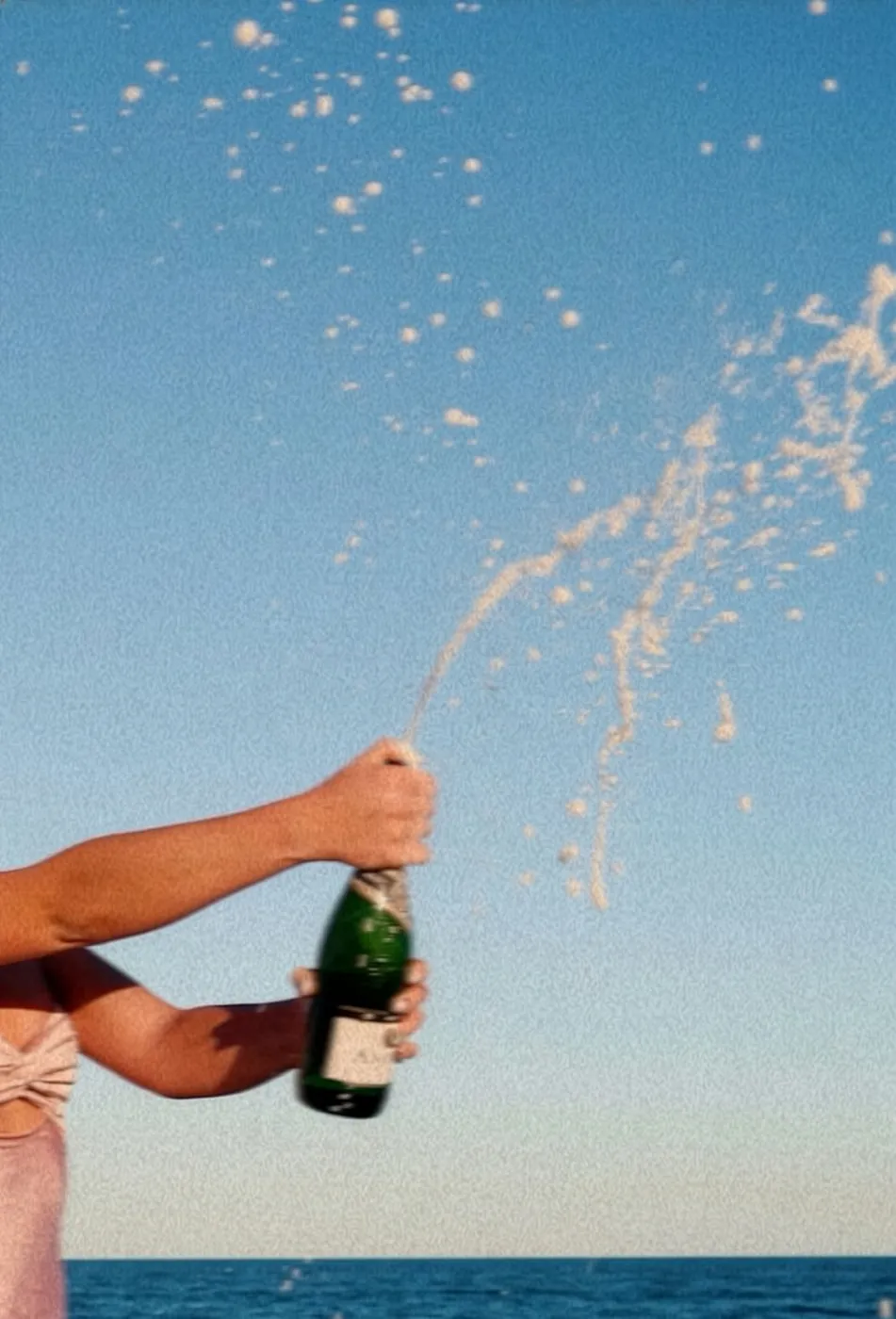 Champagne spraying into a blue sky over the water